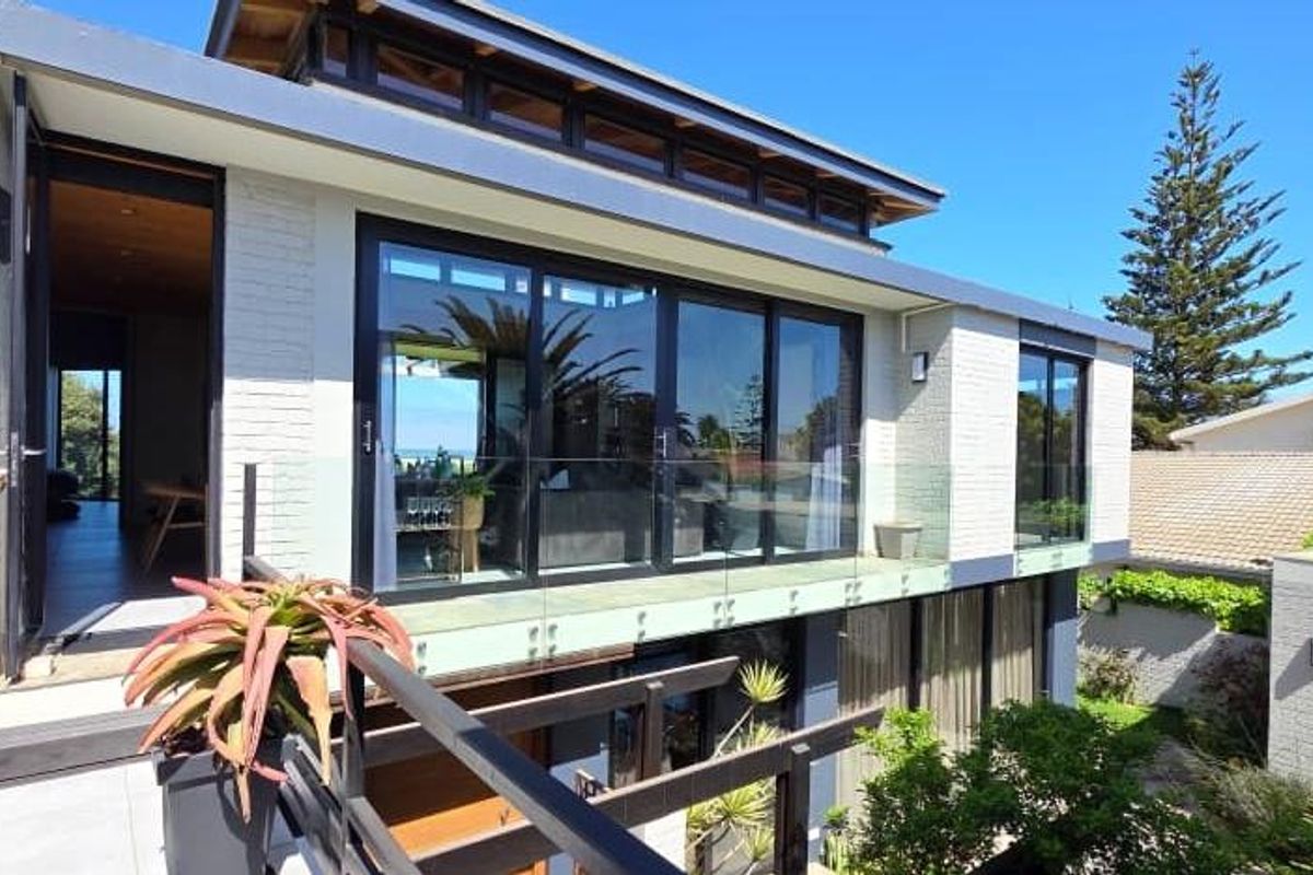 Modern rear elevation featuring a spacious balcony with glass balustrades, large sliding doors, and clerestory windows, showcasing contemporary architectural design and clean finishes.