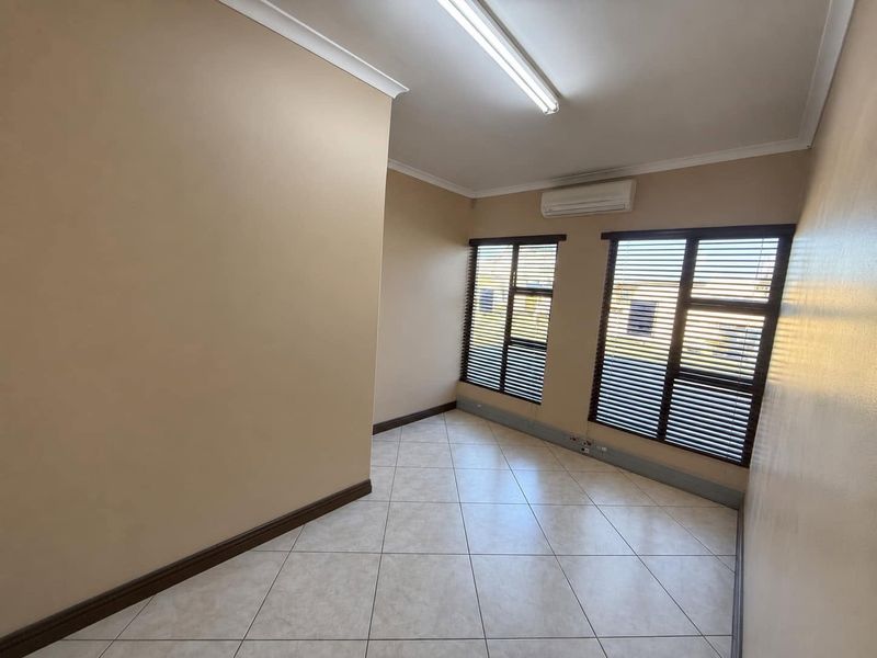 A clean, empty office space featuring tiled flooring, split-system air conditioning, and large windows with fitted venetian blinds.
