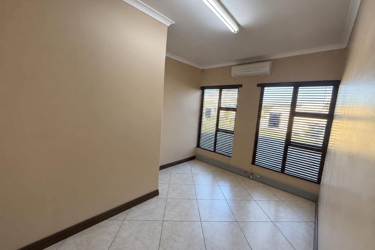A clean, empty office space featuring tiled flooring, split-system air conditioning, and large windows with fitted venetian blinds.