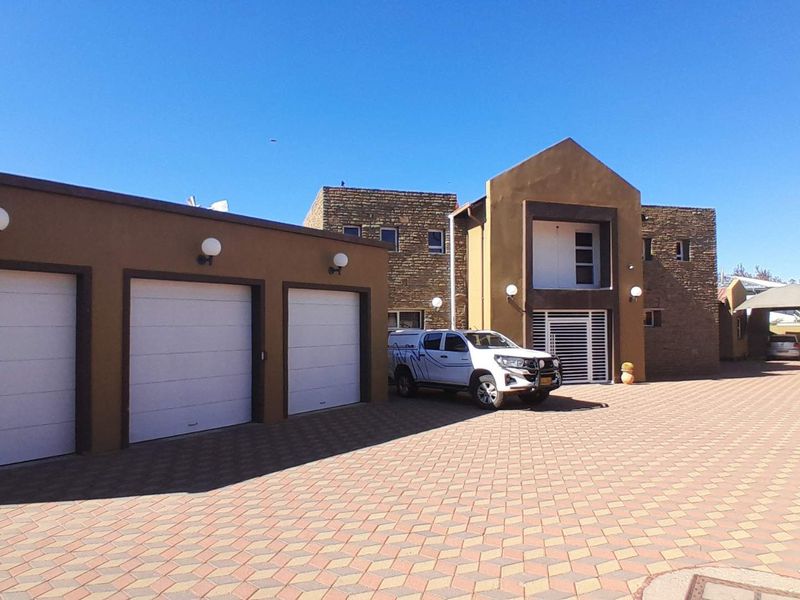 Front view of the property featuring a triple garage, extensive paved driveway, and a combination of stone and rendered exterior finishes.