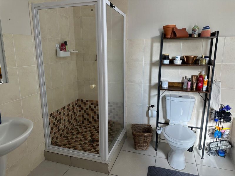 A functional bathroom featuring a corner shower enclosure with mosaic floor tiles, a standard toilet, and a pedestal basin with neutral wall tiling.