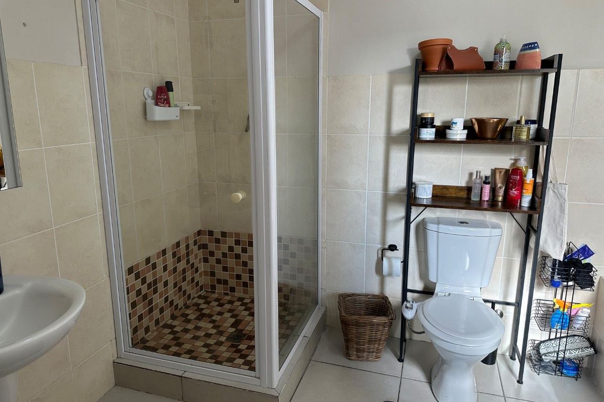 A functional bathroom featuring a corner shower enclosure with mosaic floor tiles, a standard toilet, and a pedestal basin with neutral wall tiling.