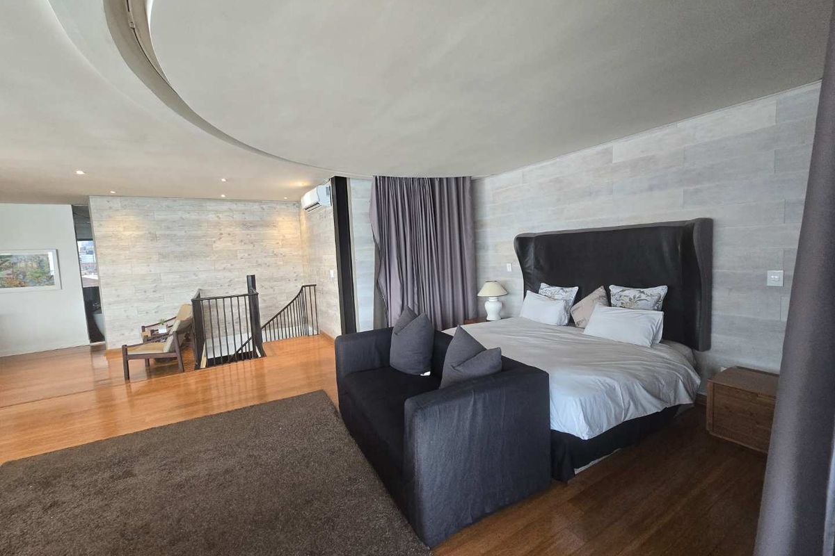 Spacious bedroom featuring hardwood flooring, a unique circular recessed ceiling detail, and an integrated staircase leading to the lower level.
