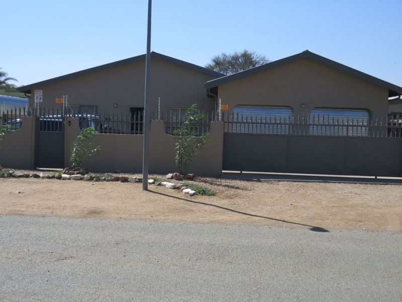 Front exterior view of the house featuring a solid boundary wall, metal security fencing, and a double garage entrance.