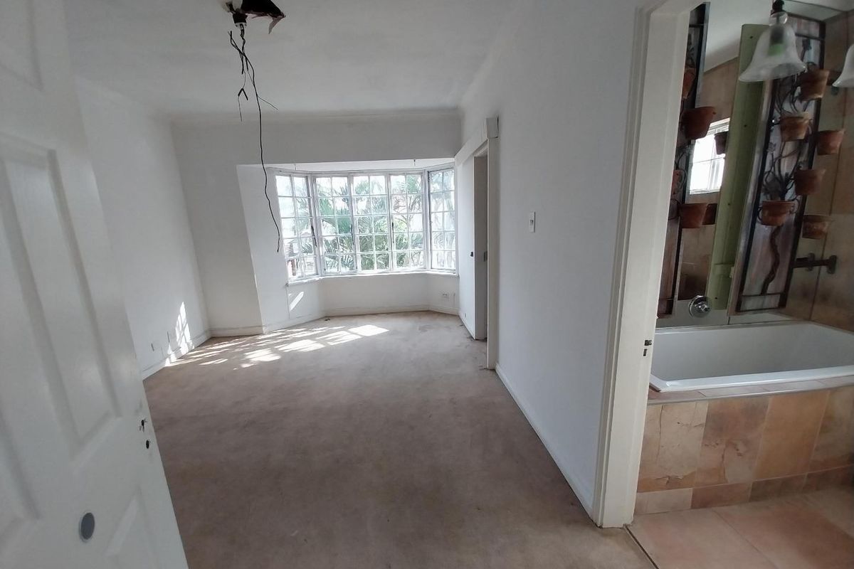 An empty bedroom featuring a bay window and an adjoining bathroom with a built-in bathtub, requiring minor electrical and flooring repairs.