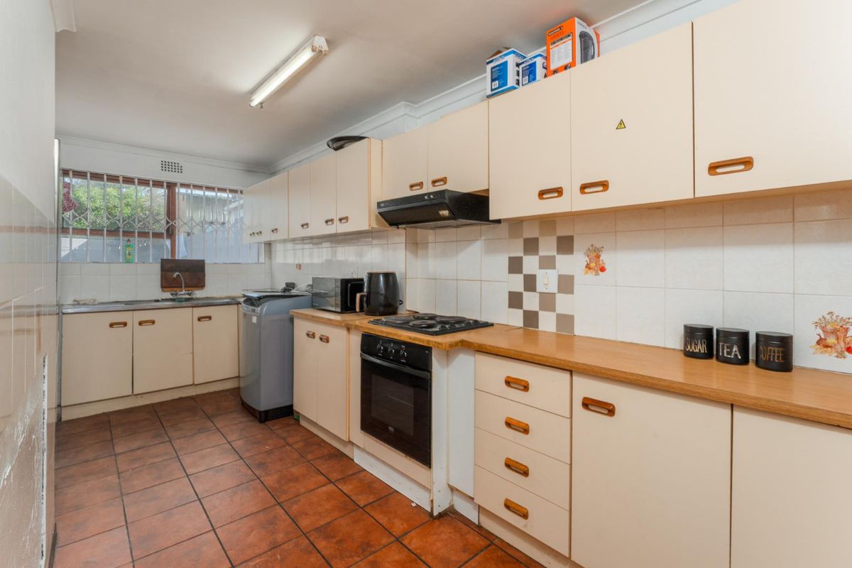 A functional kitchen featuring dated cabinetry, laminate countertops, built-in oven with gas hob, and ceramic floor tiles, offering significant potential for modernization.