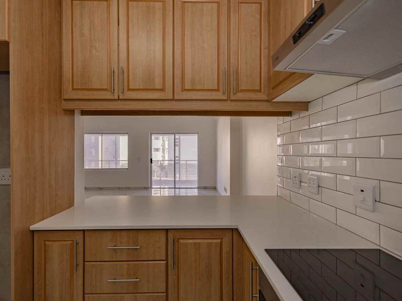 A clean, modern kitchen featuring wooden cabinetry, white subway tile backsplash, quartz countertops, and a built-in electric hob with an extractor fan.