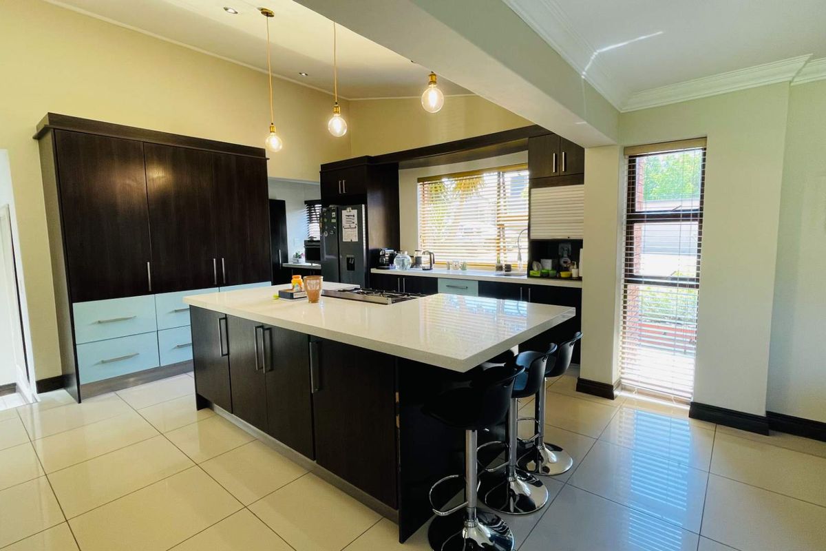Modern kitchen featuring a large central island with stone countertops, dark cabinetry, integrated appliances, and tiled flooring with ample natural light.