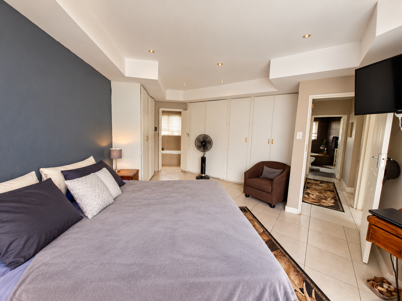 Spacious bedroom featuring built-in cupboards, recessed ceiling lighting, tiled flooring, and direct access to an en-suite bathroom.
