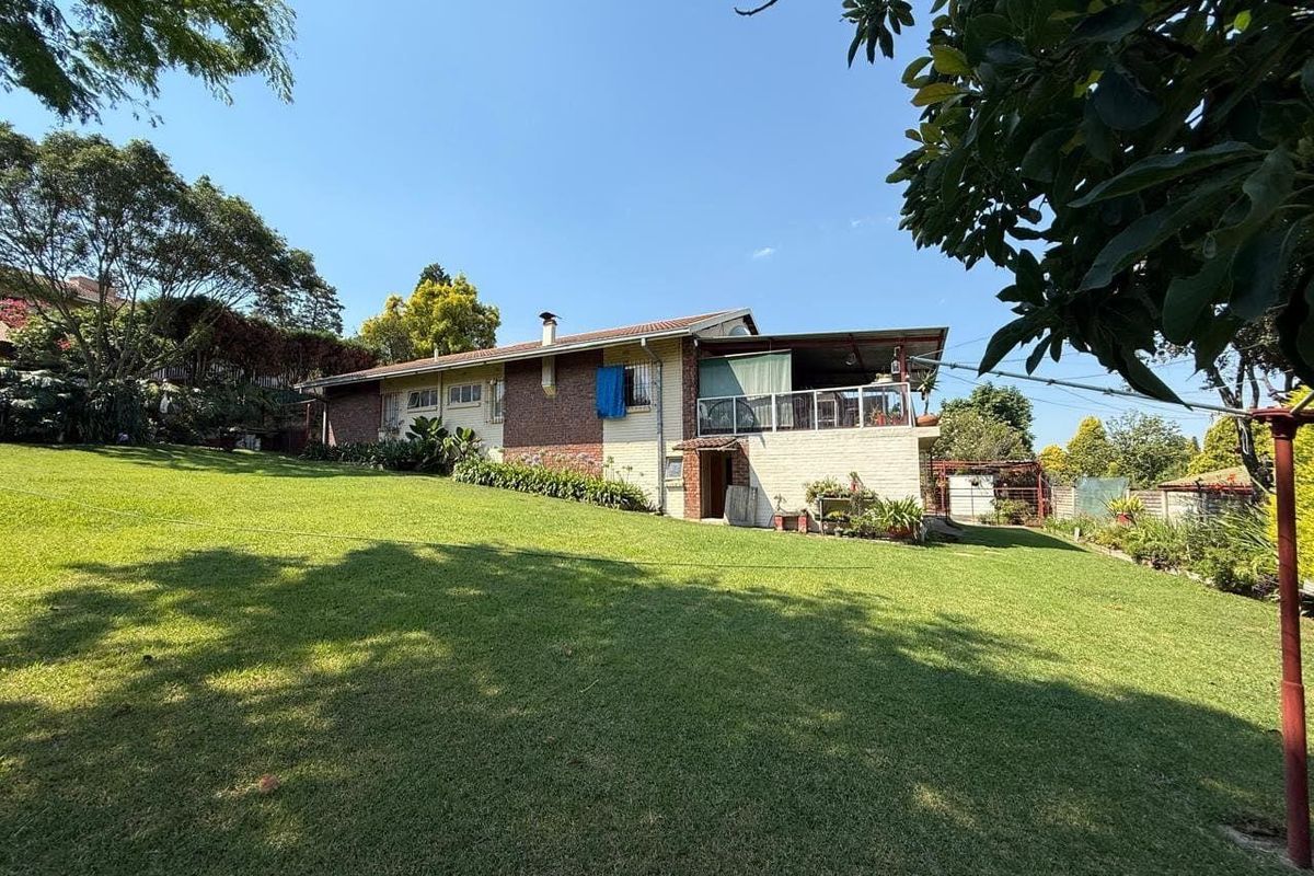 Rear view of the house featuring a spacious lawn, a covered patio area, and established garden surroundings.
