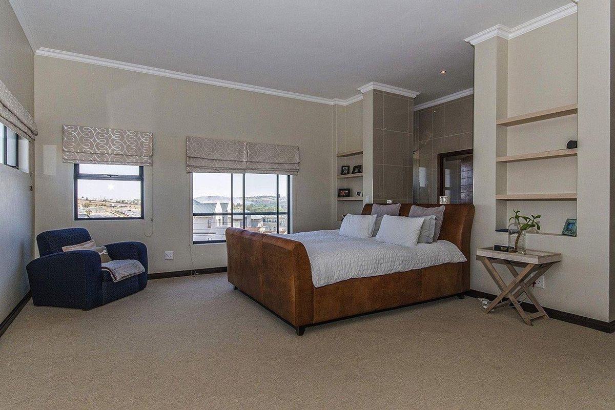 Spacious bedroom featuring neutral carpeting, built-in shelving, crown molding, and large windows with views, providing a comfortable and well-maintained living space.