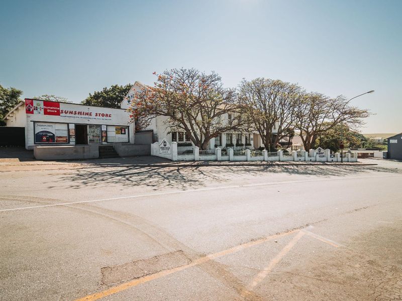 Street-level view of the commercial property frontage featuring a retail store and adjacent building with established trees and boundary walling.