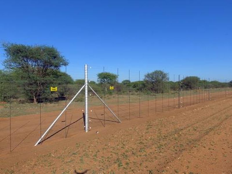 A view of the farm perimeter featuring secure wire mesh fencing with metal support posts along a dirt access road.