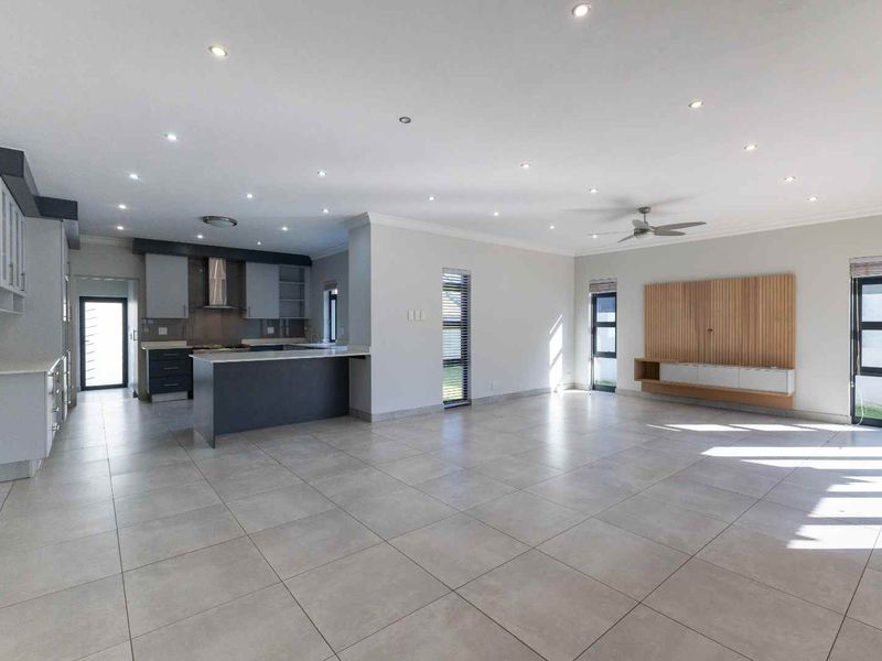 Spacious open-plan living area featuring a modern kitchen with island, tiled floors, recessed lighting, and a built-in media console.