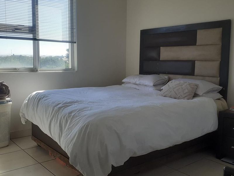 A bedroom featuring tiled flooring and a large window with venetian blinds, offering natural light and an exterior view.