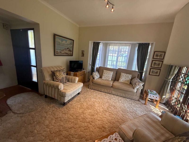 A cozy living room featuring a large bay window, security gate, and carpeted flooring, offering a comfortable and traditional living space.