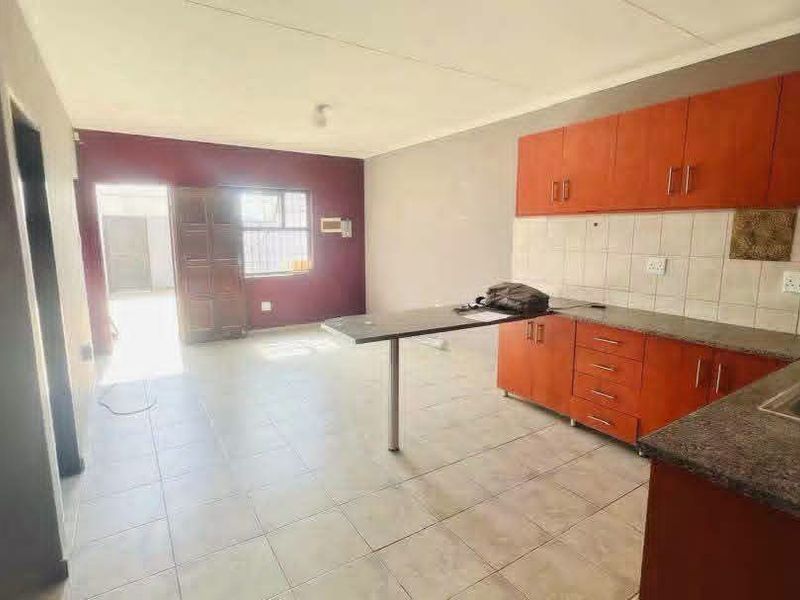 Open plan kitchen and living area featuring tiled flooring, built-in wooden cabinetry, and a breakfast counter, offering a functional and versatile living space.
