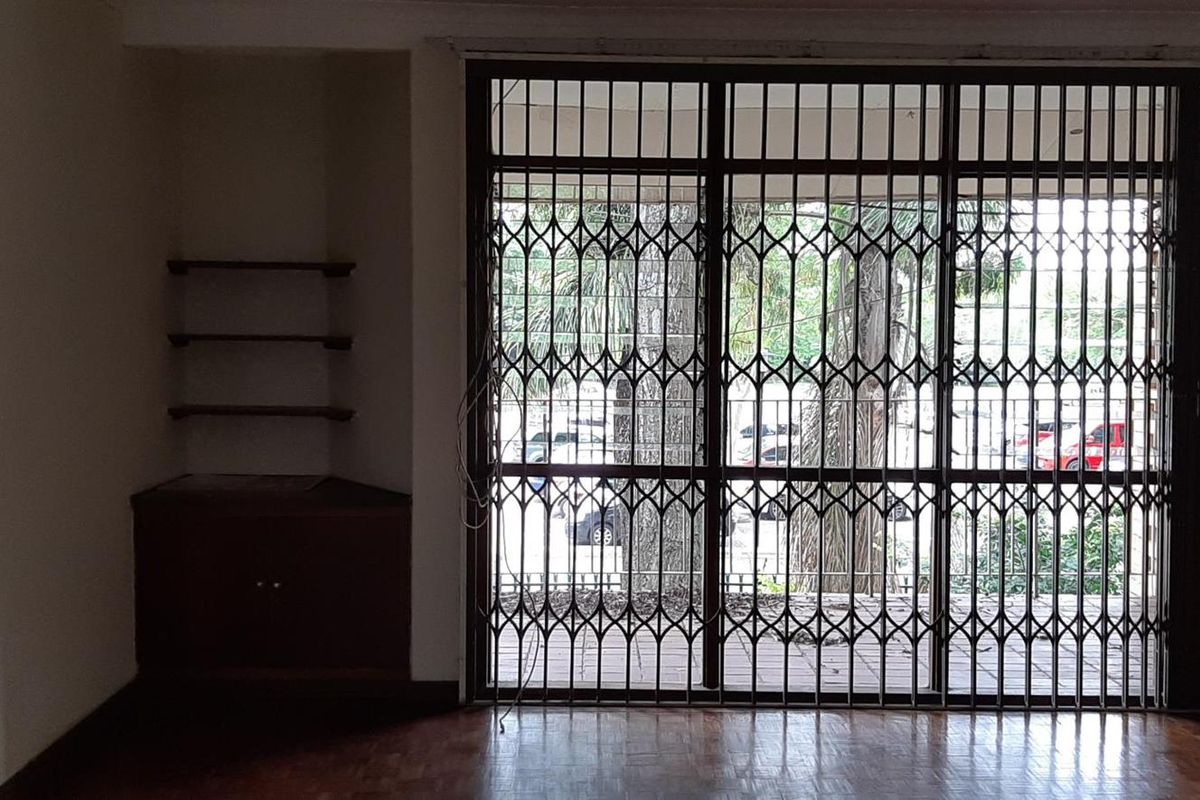 Empty living area featuring parquet flooring, built-in corner cabinetry with shelving, and a large security gate leading to the exterior.