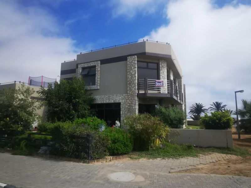 A two-story residential property featuring stone cladding accents, a balcony with metal railings, and a paved front area.