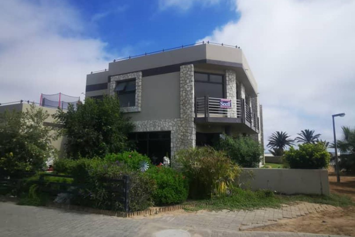 A two-story residential property featuring stone cladding accents, a balcony with metal railings, and a paved front area.