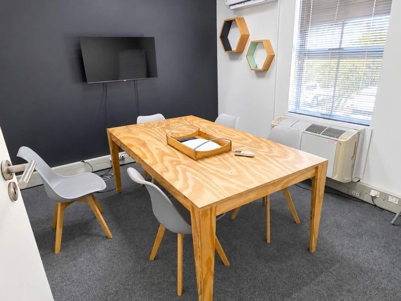 A functional office meeting room featuring carpeted flooring, an air conditioning unit, and a window with blinds.