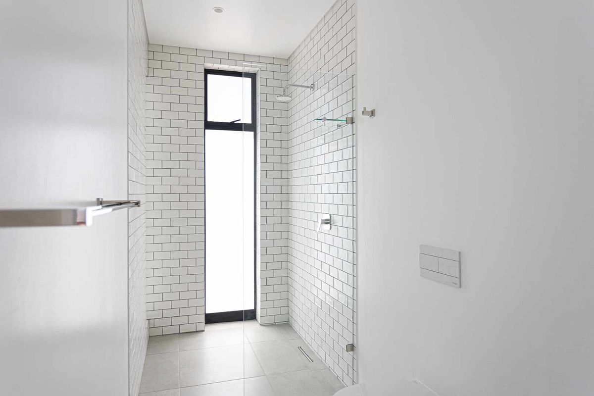 Modern bathroom featuring a walk-in shower with white subway tile walls, a glass partition, and a tall vertical window for natural light.