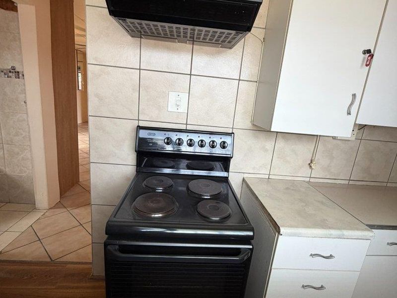 A functional kitchen area featuring a freestanding electric stove, extractor fan, tiled backsplash, and white laminate cabinetry with ample storage space.
