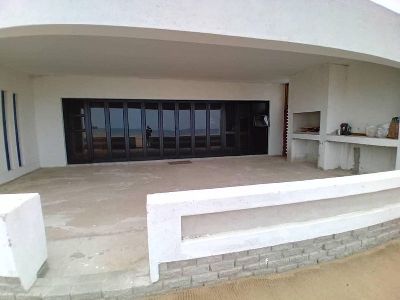 A spacious covered patio featuring a built-in braai, concrete flooring, and large folding glass doors providing seamless access to the interior living space.