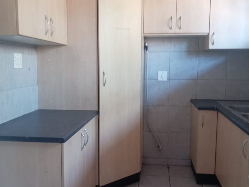 A functional kitchen featuring light wood-tone cabinetry, dark laminate countertops, tiled backsplash, and tiled flooring, offering a clean and practical workspace.