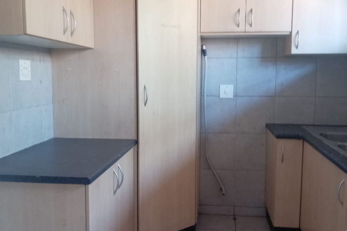 A functional kitchen featuring light wood-tone cabinetry, dark laminate countertops, tiled backsplash, and tiled flooring, offering a clean and practical workspace.
