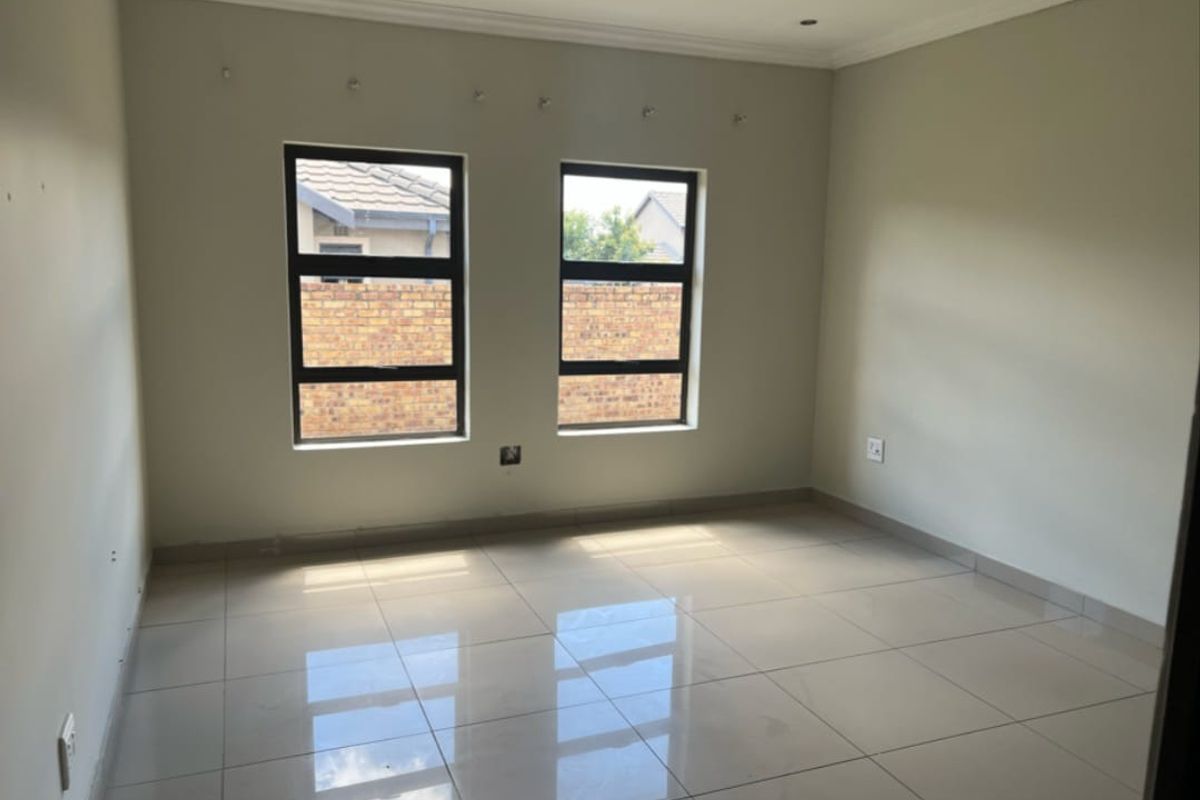 A bright, empty bedroom featuring neutral tiled flooring, clean walls, and modern aluminium-framed windows, providing a blank canvas for personalization.