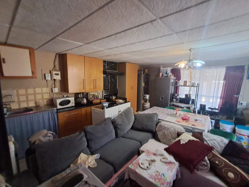 Open-plan living and kitchen area featuring dated cabinetry, tiled backsplash, and a drop ceiling, offering potential for modernization and improved layout.