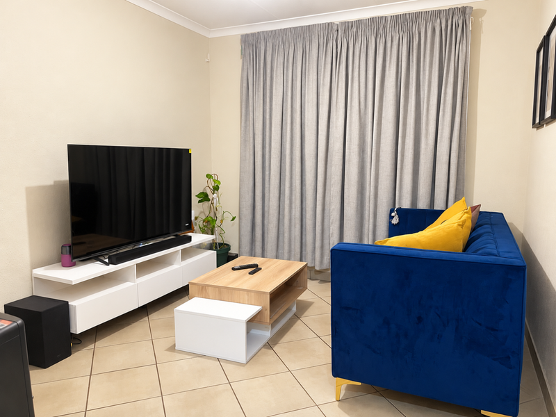 A comfortable living room featuring neutral wall tones, ceramic floor tiles, and floor-to-ceiling curtains, providing a functional and well-lit space for relaxation.
