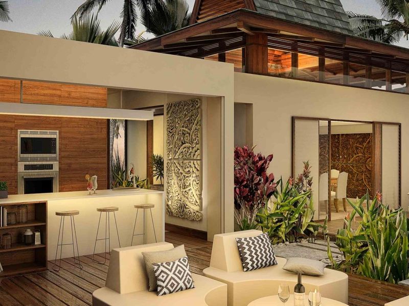 A luxurious covered outdoor patio featuring a built-in kitchen, timber decking, and seamless access to a private swimming pool area.
