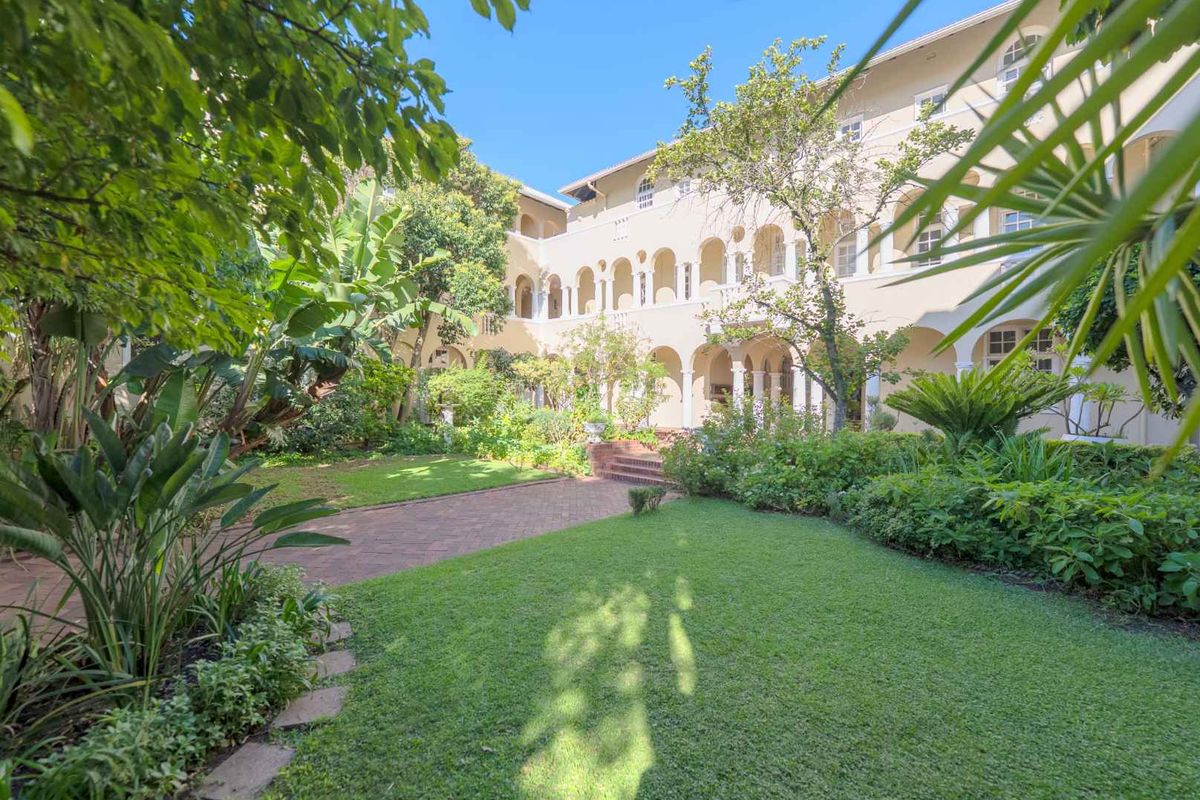 A lush, well-maintained rear garden featuring a brick pathway and a multi-story building with an elegant arched colonnade.