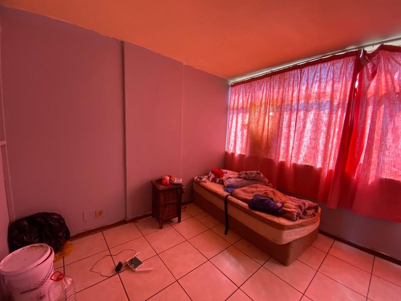 A bedroom featuring tiled flooring and a large window, currently requiring cosmetic updates and improved lighting to enhance the space.
