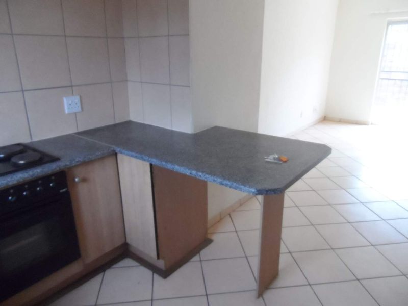 Open plan kitchen area featuring a breakfast bar, built-in oven, hob, and tiled flooring, offering a functional space ready for modern updates.