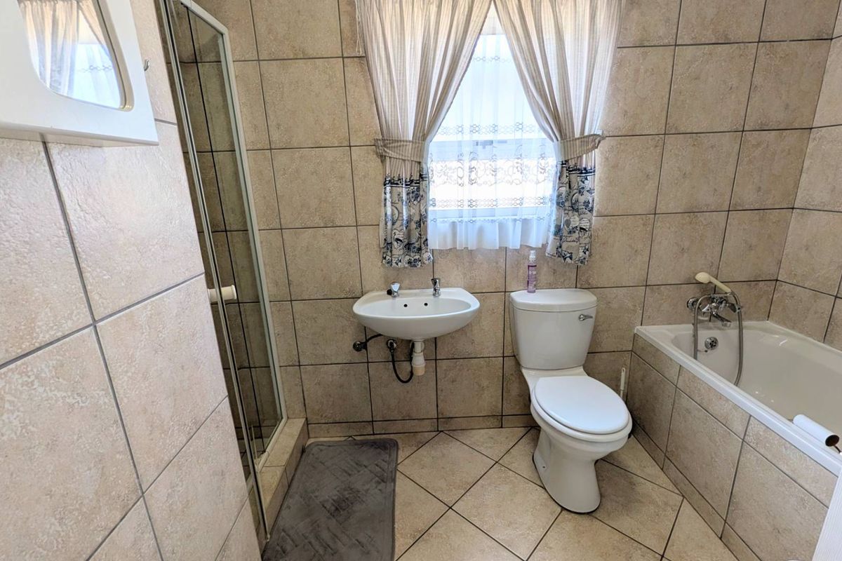 A functional bathroom featuring a wall-mounted basin, toilet, bathtub, and a separate shower enclosure with neutral floor-to-ceiling tiling.
