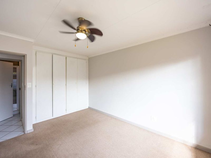 A clean, empty bedroom featuring neutral carpeting, built-in cupboards, and a ceiling fan, offering a blank canvas for personalization.