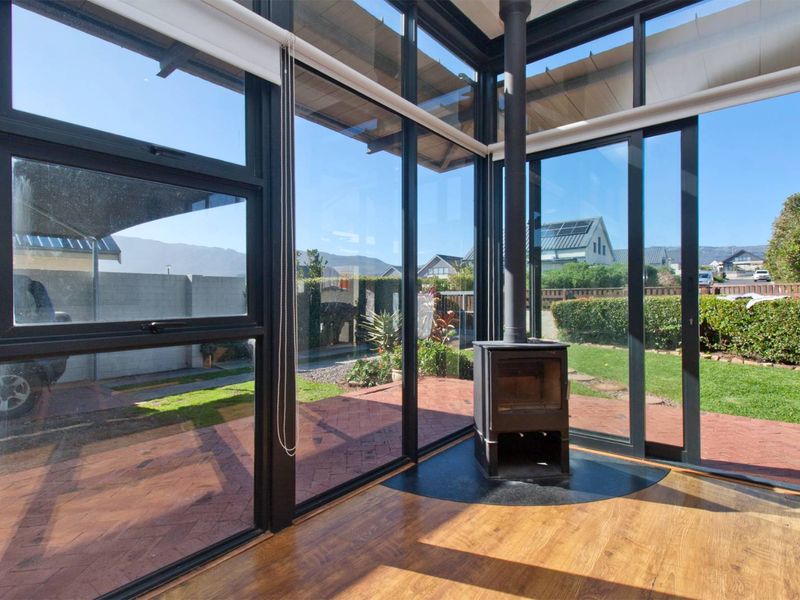 Bright living area featuring floor-to-ceiling windows, sliding glass doors to the patio, and a central freestanding fireplace on a hearth.
