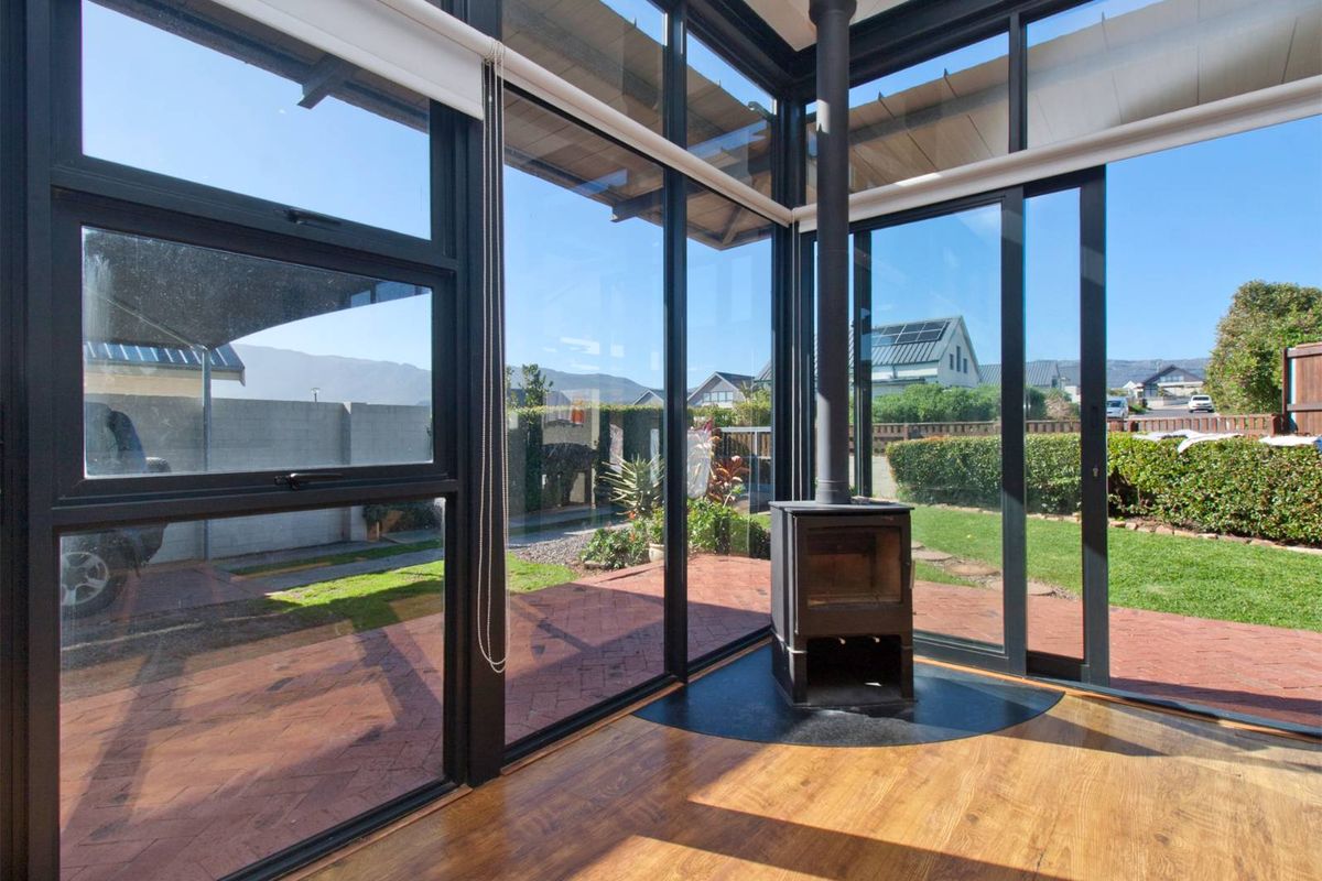 Bright living area featuring floor-to-ceiling windows, sliding glass doors to the patio, and a central freestanding fireplace on a hearth.