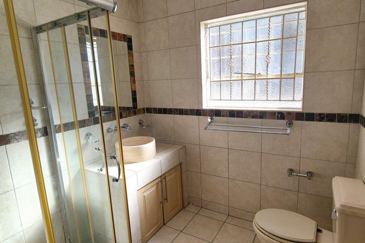 A functional bathroom featuring a tiled shower enclosure, a vessel sink vanity, and a window with security bars.