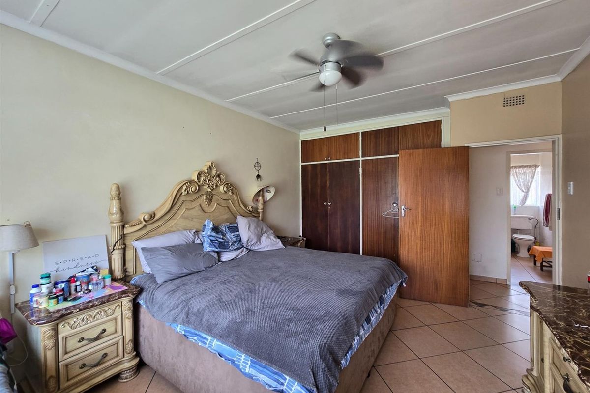 A bedroom featuring built-in wooden cupboards, a ceiling fan, and tiled flooring, with an adjoining view into a bathroom area.