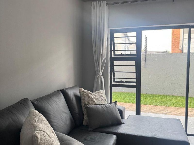 A modern living room featuring laminate flooring and a large sliding glass door providing access to an outdoor patio area.
