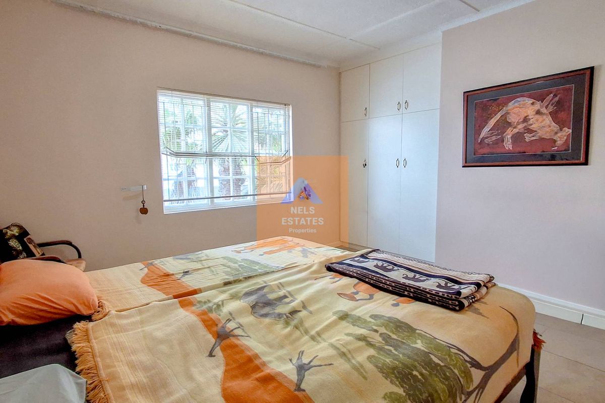 A functional bedroom featuring built-in cupboards, tiled flooring, and a window with fitted blinds, offering a neutral space ready for personalization.