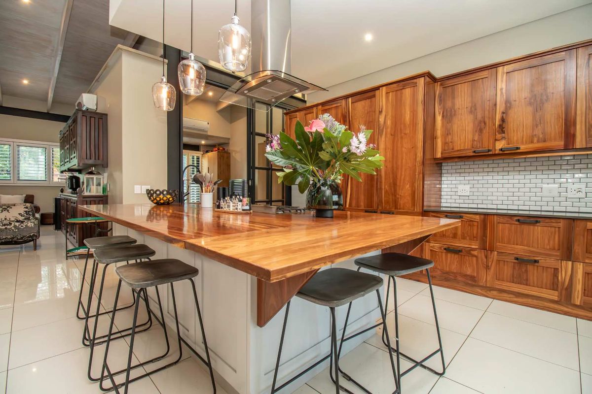 Modern kitchen featuring warm wood cabinetry, a large central island with a timber countertop, subway tile backsplash, and stainless steel extractor fan.