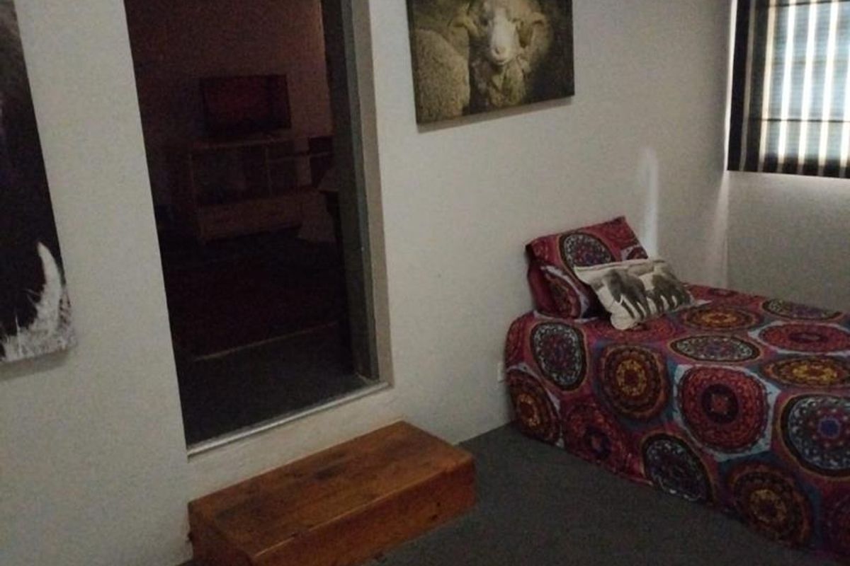 A bedroom featuring neutral walls, carpeted flooring, and window roller blinds, with a doorway leading to an adjacent room.