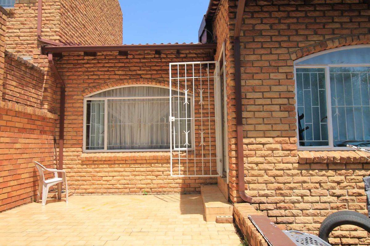 A rear exterior view of the townhouse featuring exposed face-brick walls, paved patio area, and security gates on windows and doors.