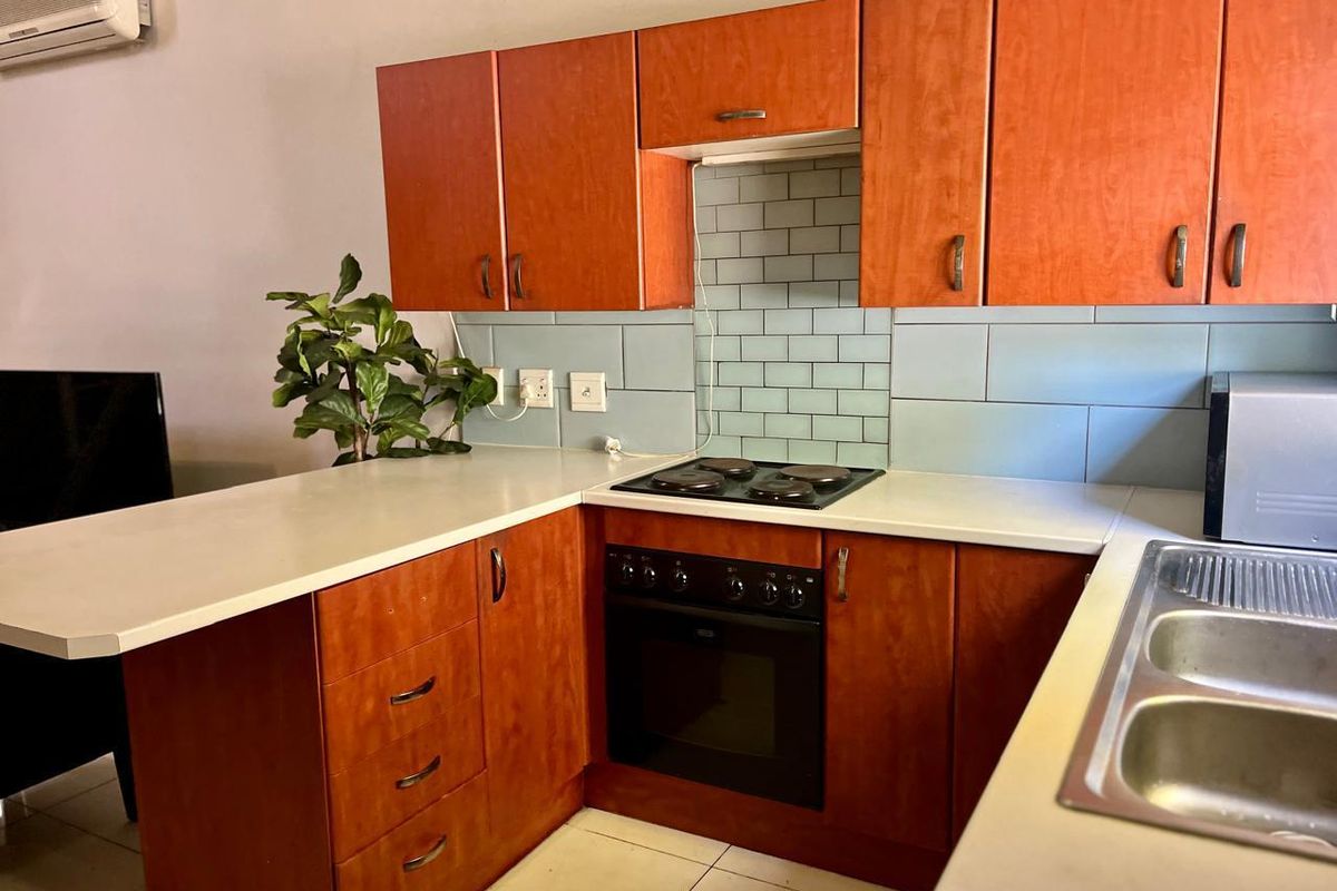 A functional kitchen featuring wood-tone cabinetry, a built-in oven with electric hob, subway tile backsplash, and a double-basin stainless steel sink.