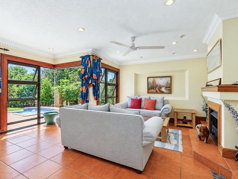 Spacious living room featuring a fireplace, tiled flooring, and large corner windows providing views of the outdoor pool area.
